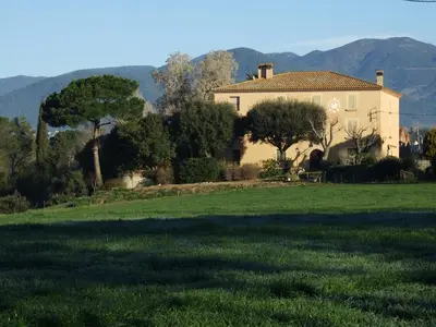 a house in a field with mountains in the background at Hotel Can Ribalta in San Antonio de Vilamajor