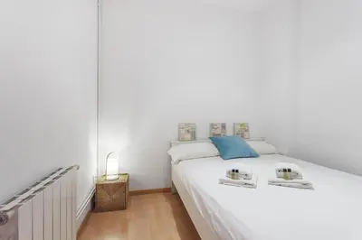 a white bedroom with a large white bed with blue accents at Flateli Aribau in Barcelona