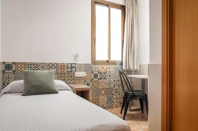 a bedroom with a bed and a window and a chair at Hostal Baler in Barcelona