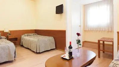 a room with two beds and a table with a bottle of wine at Hostal Oliva in Barcelona