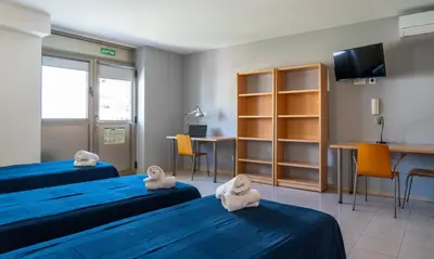a room with two beds and a table and a desk at Apartaments Turístics Residencia Vila Nova in Vilanova i la Geltrú