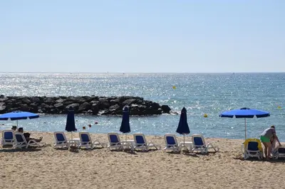 a group of chairs and umbrellas on a beach at Apartamentos Les Barbes in Caldes d'Estrac