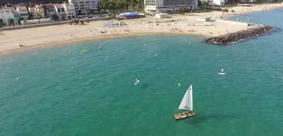 a sail boat in the water next to a beach at Apartamentos Les Barbes in Caldes d'Estrac
