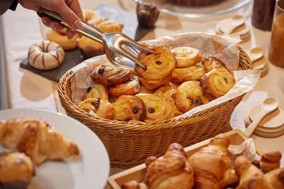 a basket of pastries on a table with a person holding a spoon at Barcelona Century Hotel in Barcelona