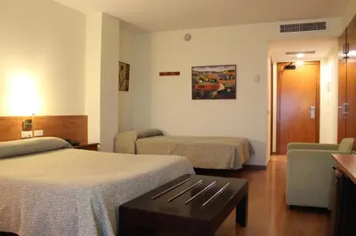 a hotel room with two beds and a chair at Hotel Flora Parc in Castelldefels