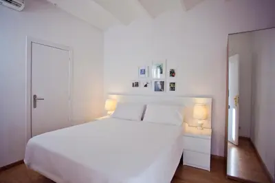 a white bedroom with a white bed and two lamps at Ramblas Apartments in Barcelona