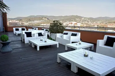 a patio with white chairs and tables on a roof at Hotel Badalona Tower in Badalona