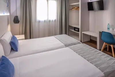 a bedroom with a large white bed with a blue chair at Hostal Operaramblas in Barcelona