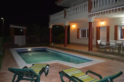 a swimming pool with chairs and a house at night at Vista Cunit in Cubelles