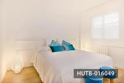 a white bedroom with a white bed with blue pillows at Elegant Sitges Apartment in Sitges