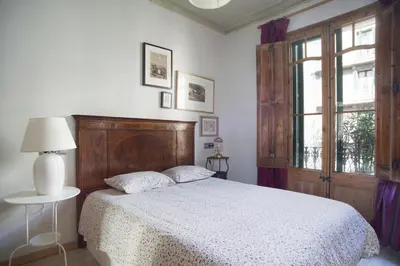 a bedroom with a bed with a wooden headboard and a window at ApartEasy - Authentic Family Apartment in Barcelona