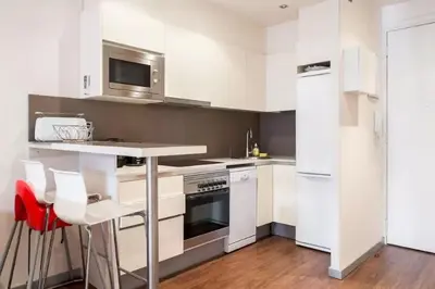 a white kitchen with white cabinets and a red stool at Tendency Plaza España in Barcelona