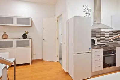 a white kitchen with a refrigerator and a table at Alcam Paseo San Juan in Barcelona