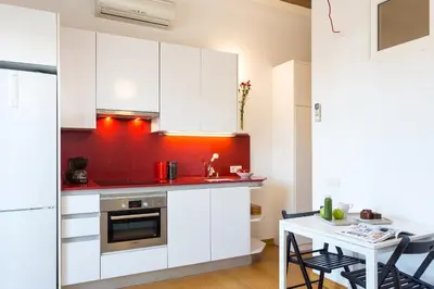 a kitchen with white cabinets and a red wall at Casa Cosi Sant Antoni in Barcelona