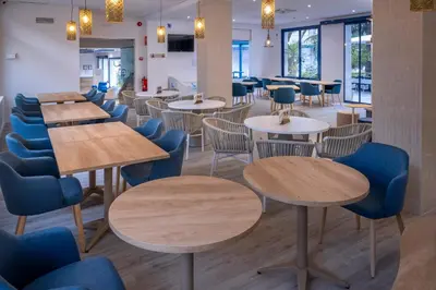 a restaurant with wooden tables and blue chairs at GHT Balmes, Hotel-Aparthotel&SPLASH in Calella