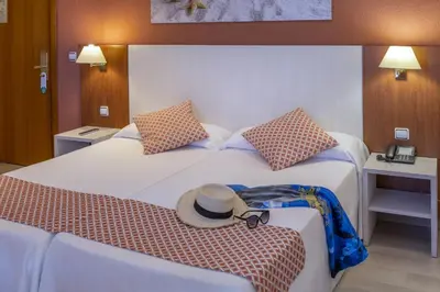 a hotel room with two beds with a hat on a bench at GHT Balmes, Hotel-Aparthotel&SPLASH in Calella