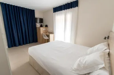 a bedroom with a white bed and blue curtains at Aparthotel Solifemar in Castelldefels