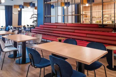 a cafeteria with tables and chairs and a large red bench at B&B HOTEL Barcelona Rubí in Rubí