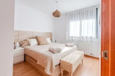 a white bedroom with a large bed and a window at Capricho Apartamento Sitges in Sitges