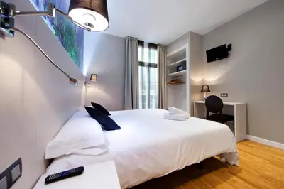 a bedroom with a white bed and a desk with a chair at Hostal BCN Ramblas in Barcelona
