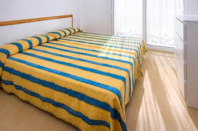 a bed with a yellow and blue striped blanket on it at Apartments Sorrabona in Pineda de Mar