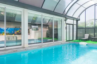 an indoor swimming pool with glass walls and a house at Luxurious Villa Marly II piscina climatizada in Castelldefels