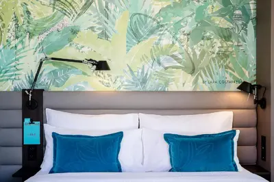 a bedroom with a bed with blue pillows and a mural at Motel One Barcelona-Ciutadella in Barcelona