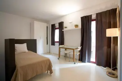 a bedroom with a bed and a table and windows at Old City Beach House in Barcelona