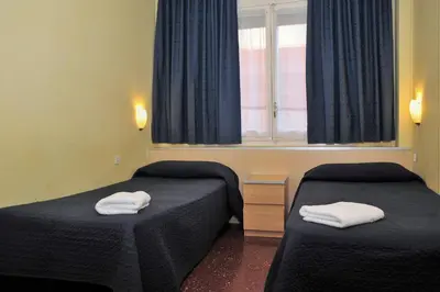 a room with two beds and a window with blue curtains at Hostal Bejar in Barcelona