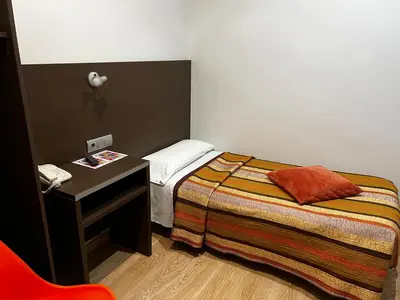 a small room with a bed and a table with a phone at Ciudad Condal Hostal - Paseo de Gracia in Barcelona