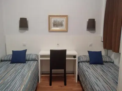 a room with a desk and two beds with blue pillows at Hostal Lesseps in Barcelona