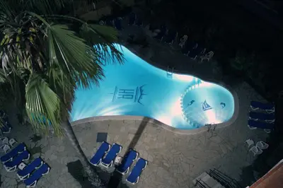 an overhead view of a swimming pool at night with blue chairs at Rocatel in Canet de Mar