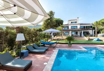 a swimming pool with chairs and an umbrella next to a house at Villa Costa Barcelona in Arenys de Munt