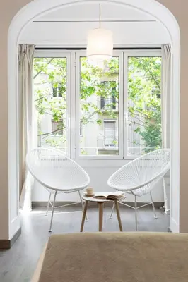 two white chairs and a table in a room with windows at KeyFamily Cozy Home in Barcelona