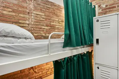 a bed in a room with a brick wall and green curtains at Hola Hostal Collblanc in Hospitalet de Llobregat