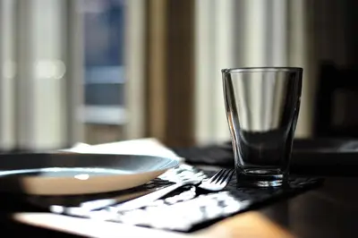 a glass on a table with a plate and a fork at Apartamentos Bejar in Barcelona