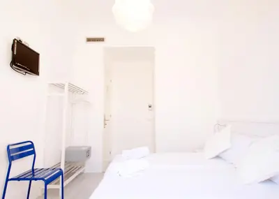 a white bedroom with a blue chair and a bed at Express by gaiarooms in Barcelona