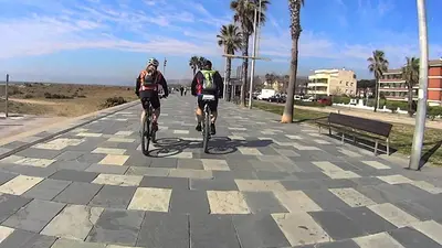 two people riding bikes down a road near the beach at Family Deluxe Apartment Beach in Castelldefels