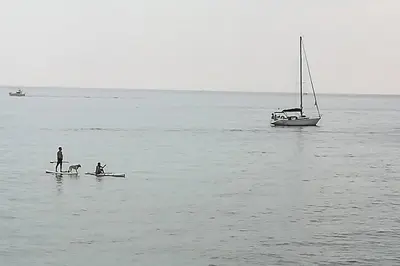 two people and a dog on a board in the water with a boat at Terrassa de Mar Apartment in Masnou