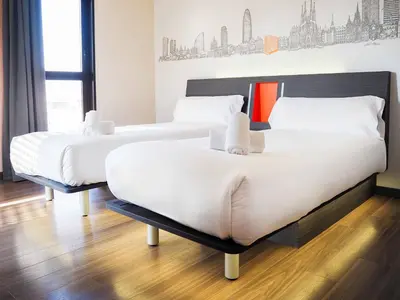 two beds in a hotel room with white sheets at easyHotel Barcelona Fira in Hospitalet de Llobregat