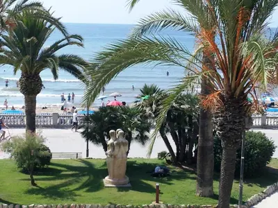 a statue in a park near a beach with palm trees at Apartament Mare Nostrum in Sitges