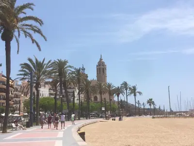a building with a clock tower on a beach with palm trees at Heart of Sitges in Sitges