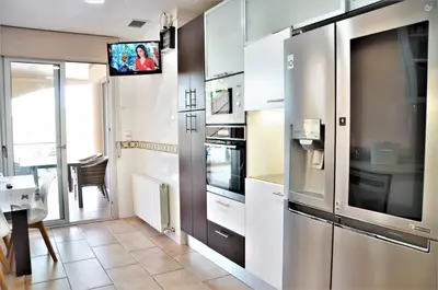 a kitchen with white cabinets and a tv on the wall at VILLA SOFIA CALELLA in Calella