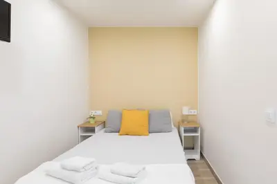a white room with a bed with a yellow pillow at Hostal Oliveta in Barcelona