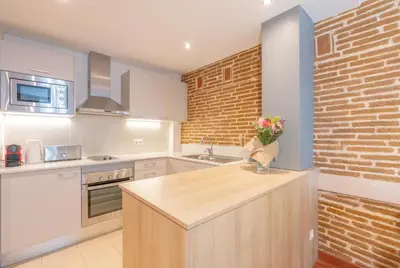 a kitchen with white cabinets and a brick wall at Serennia Cest Apartamentos Arc de Triomf in Barcelona