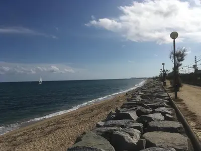a beach with rocks and a sail boat in the water at Apartament Cal Negre in Vilassar de Mar