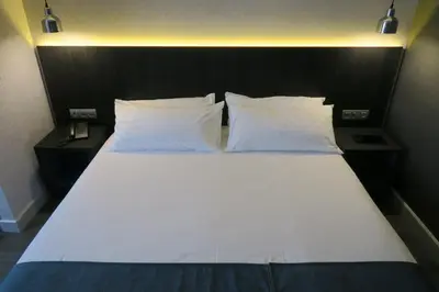 a bed with white sheets and pillows in a room at Hg City Suites Barcelona Apartments in Barcelona