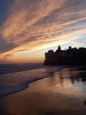 a sunset on the beach with a building in the background at Apartamento con Licencia en Sitges in Sitges