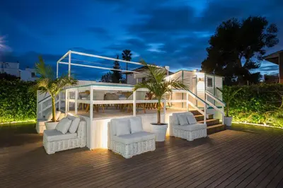 a deck with white furniture and palm trees at night at Antonio's House in Sitges