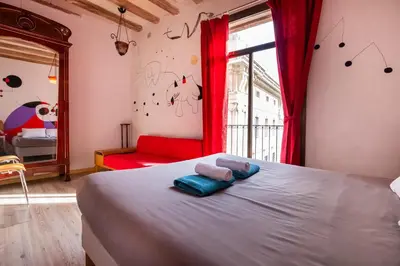 a bedroom with a bed and a red chair and a window at Apartamentos El Pintor in Barcelona